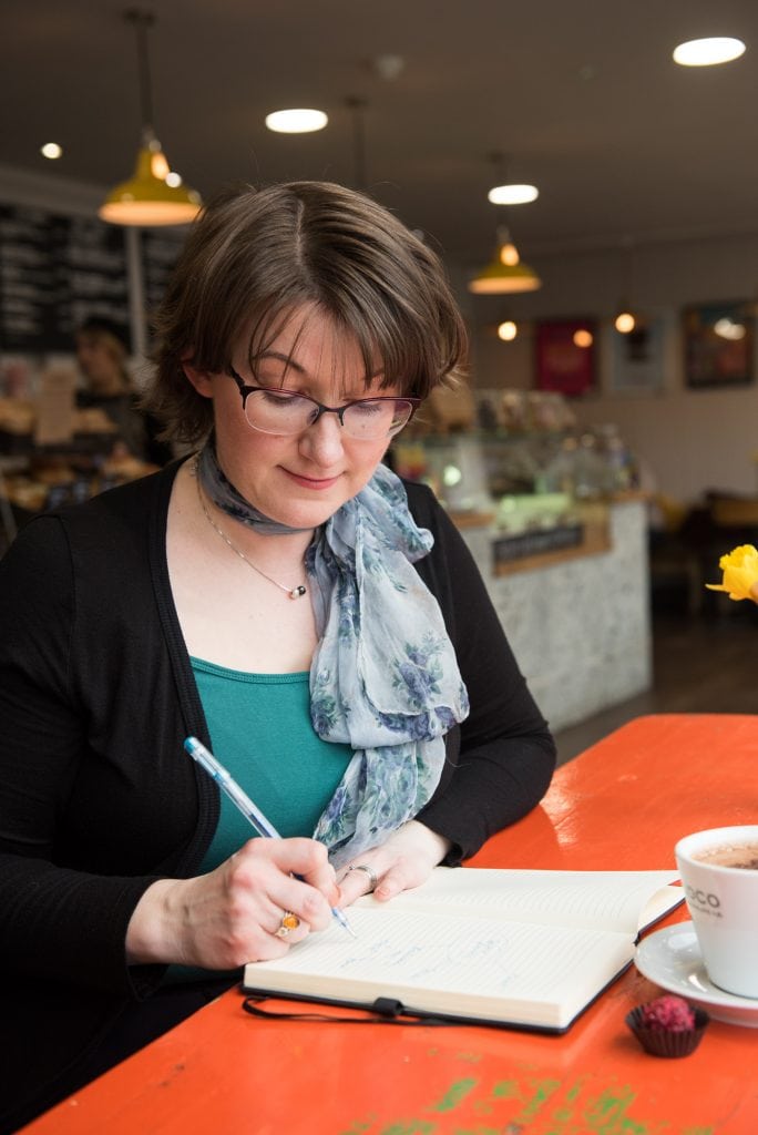 Elizabeth Harrin sitting in a cafe, writing in a notebook